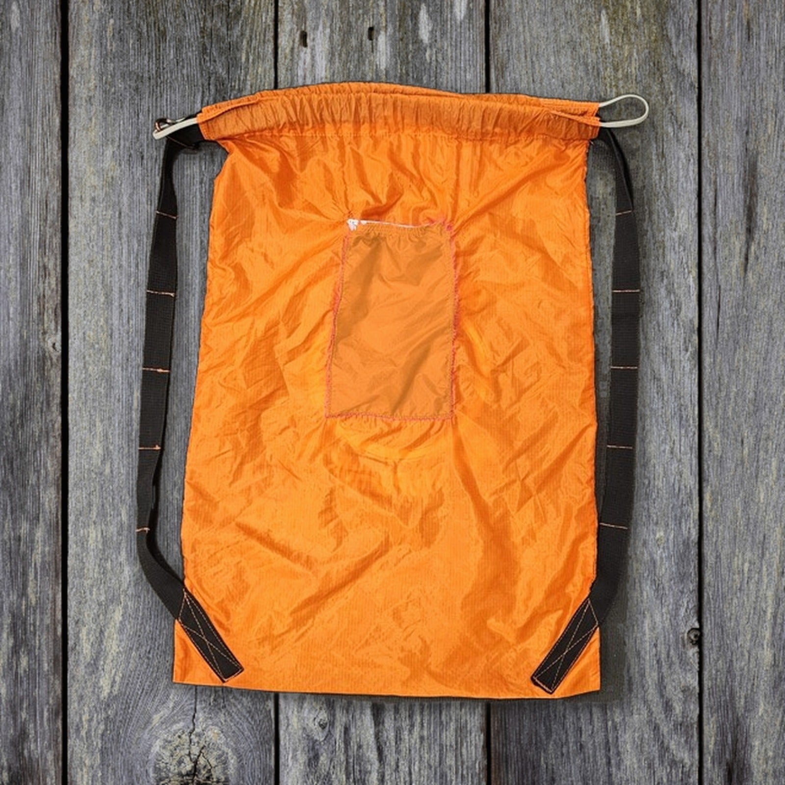 Back of drawstring bag with pocket and both straps, on weathered wood